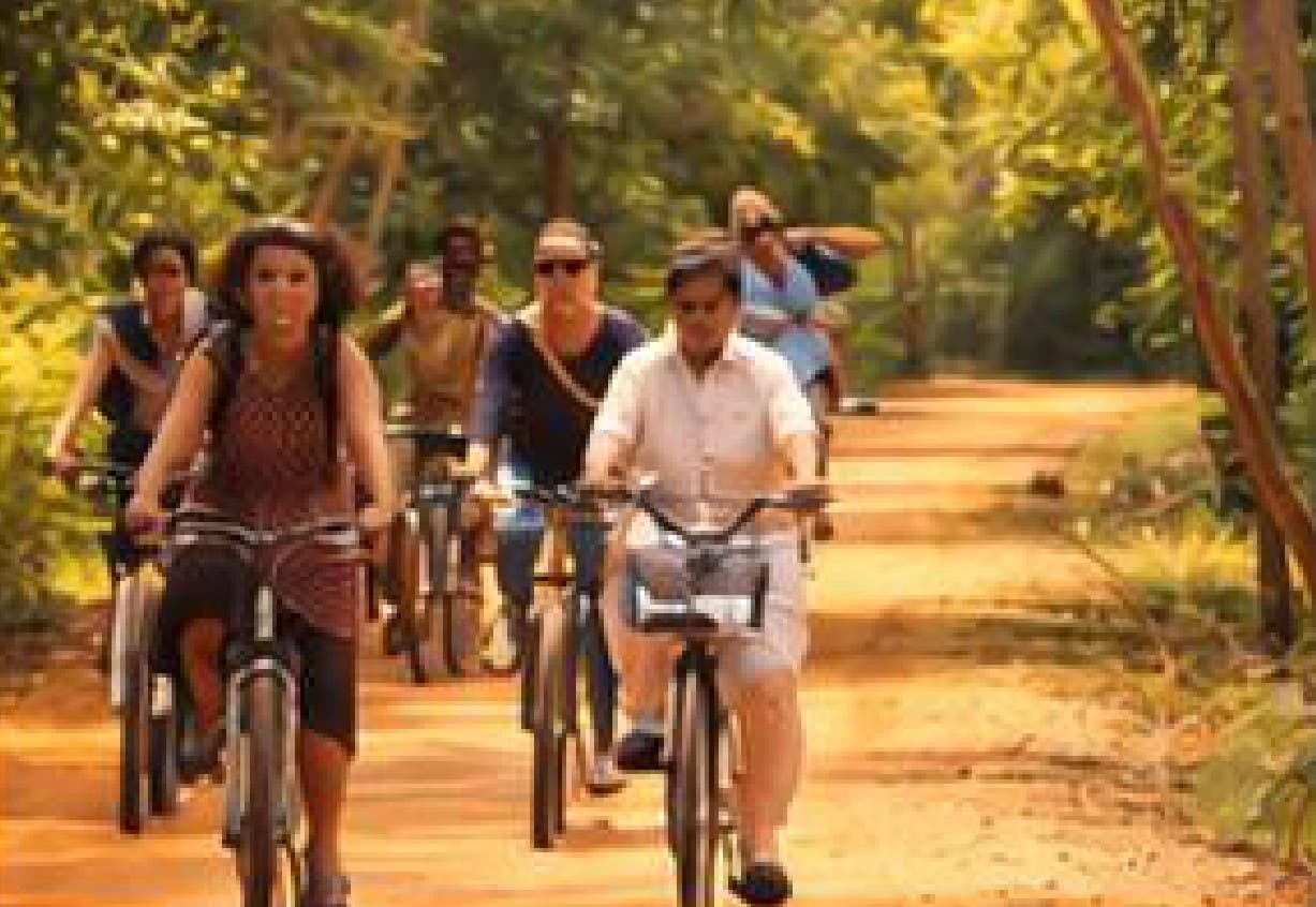 A group cycling along a red-earth forest trail in Auroville.