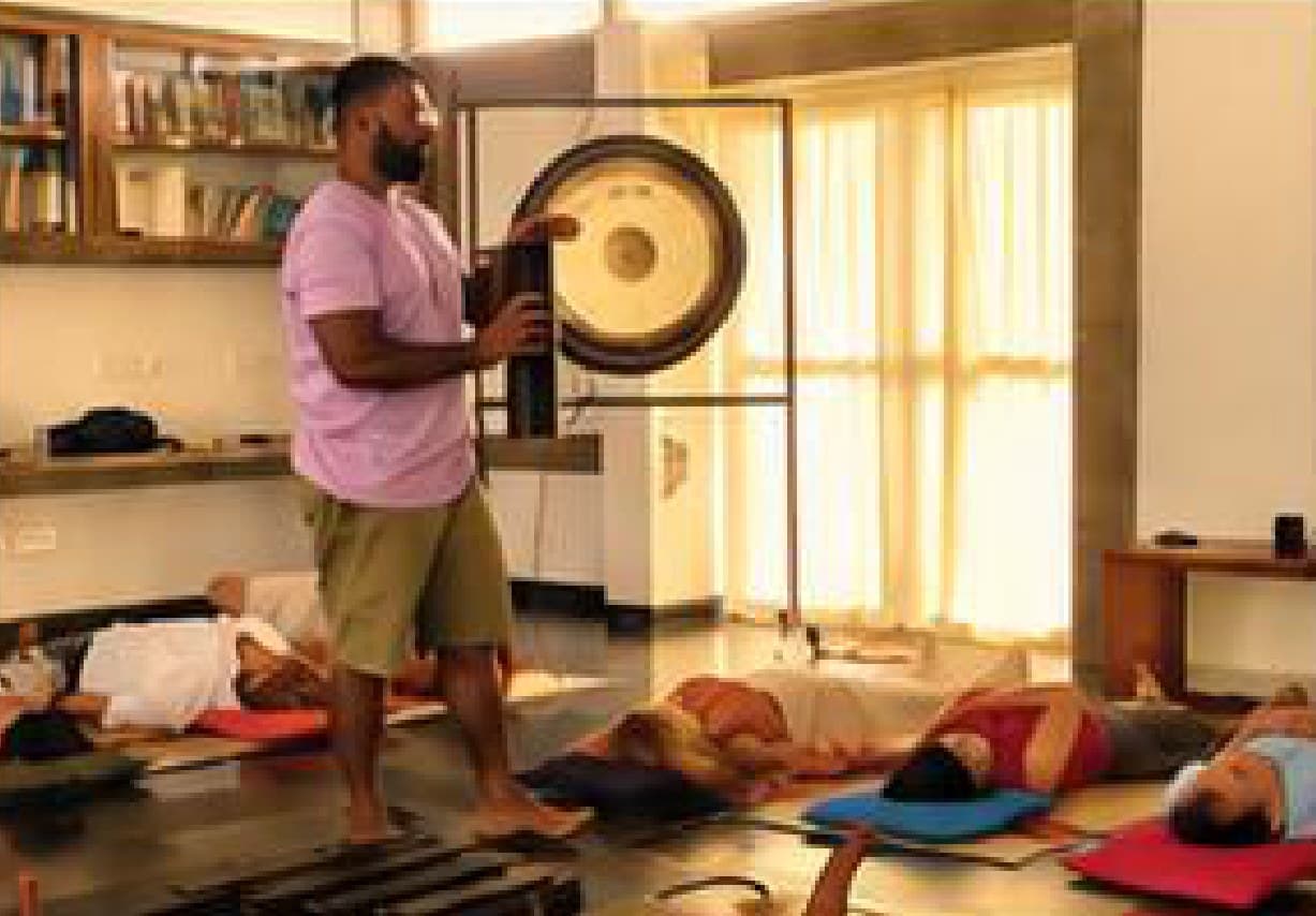A sound healer playing a gong during a SVARAM sound bath session.